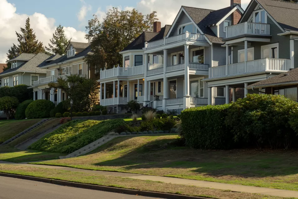 Row of large multistory homes with multilevel porches on the front and a bike lane on the street in front of them.